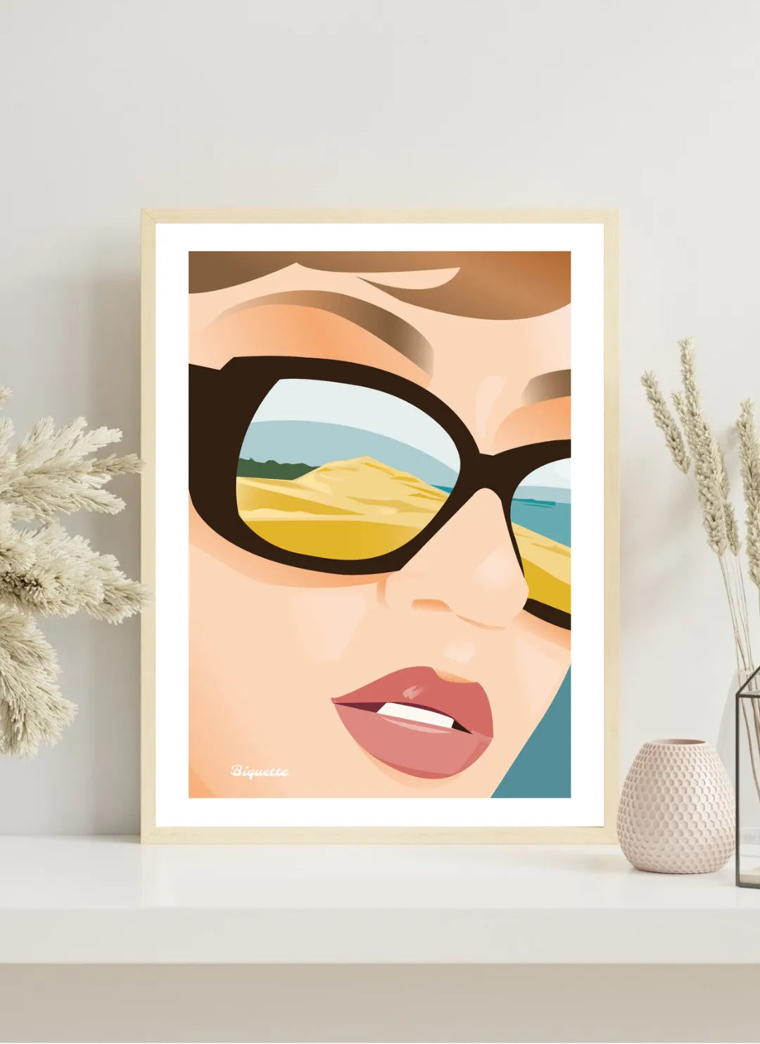 Mise en situation d'un poster Dune du Pilat dans un cadre en bois naturel, disposé sur une console blanche moderne avec des vases en céramique et une herbe de la pampa.