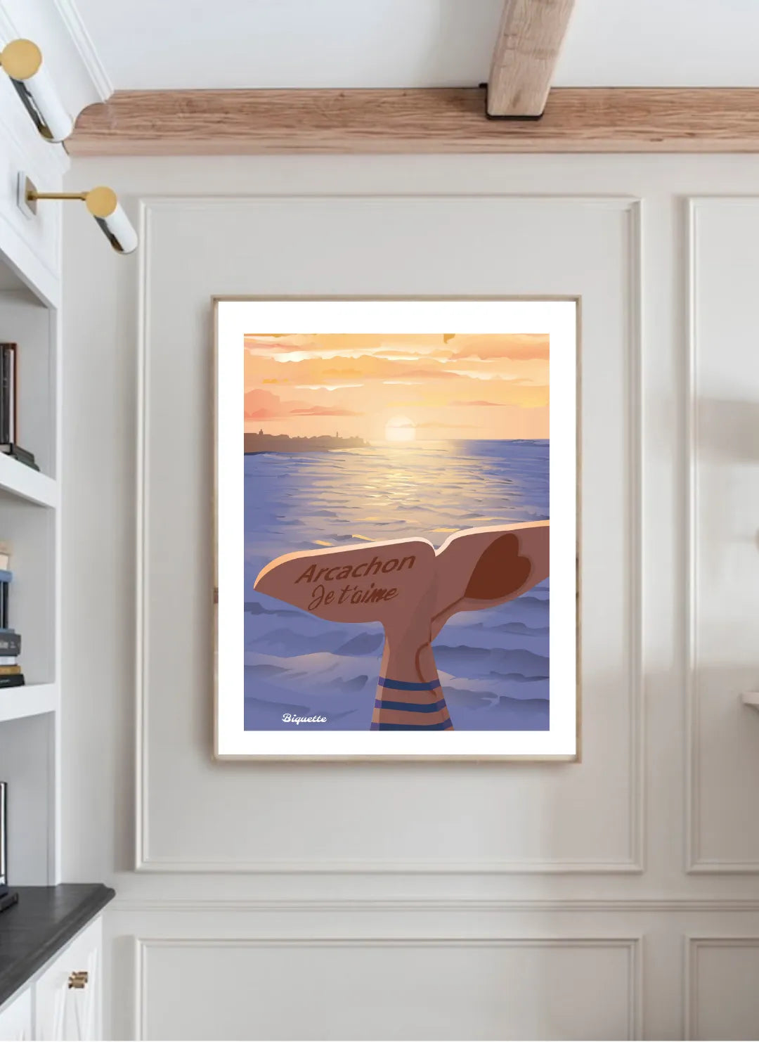 Vue d'une affiche encadrée "Arcachon Je t'aime" parfaitement intégrée dans un panneau mural à moulures sous une poutre en bois apparente, soulignant le cachet de la pièce.