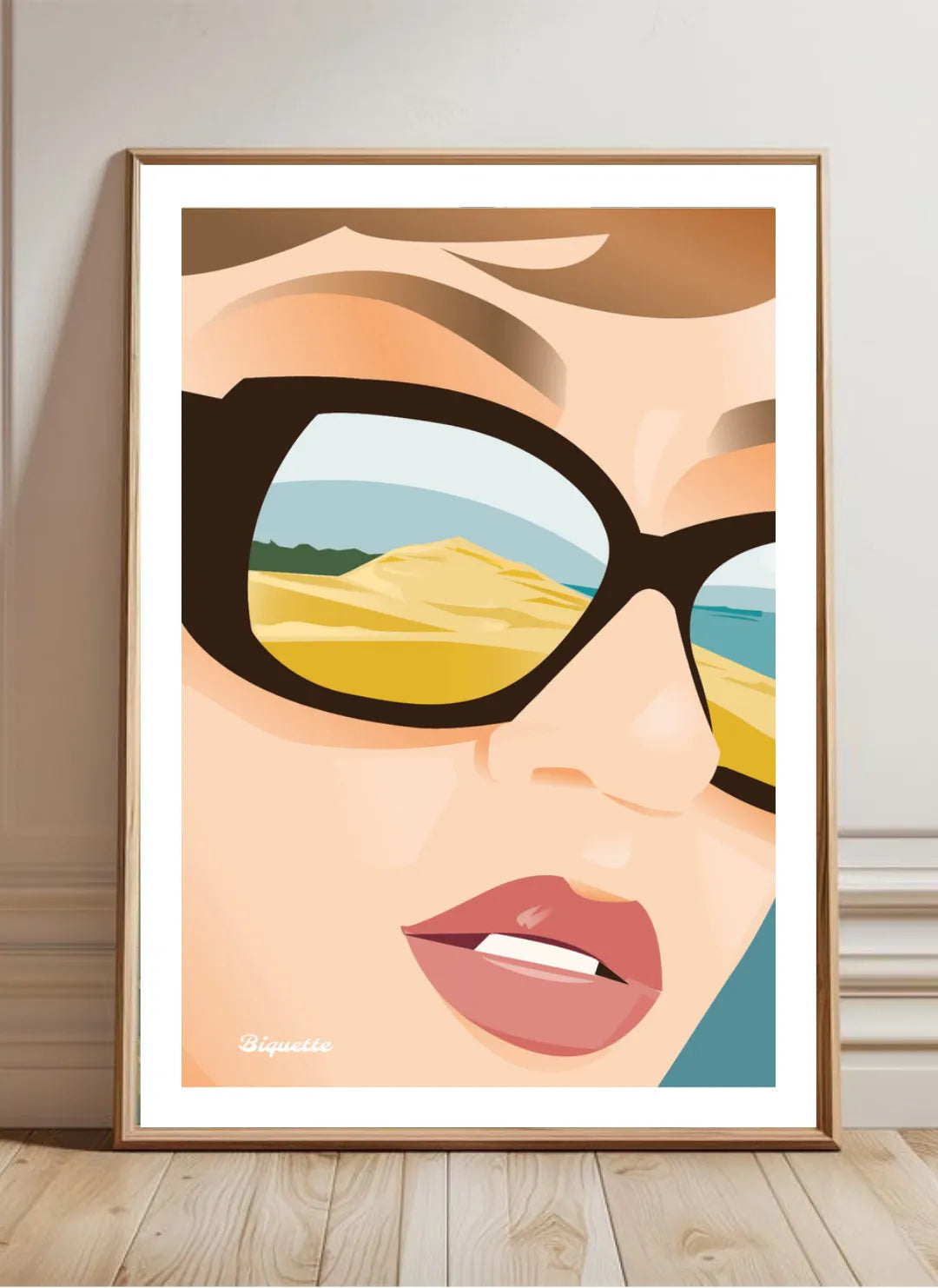 Illustration de la Dune du Pilat sous cadre en bois clair, posée au sol contre un mur blanc élégant avec moulures et parquet en chevrons, style décoration chic et lumineuse.
