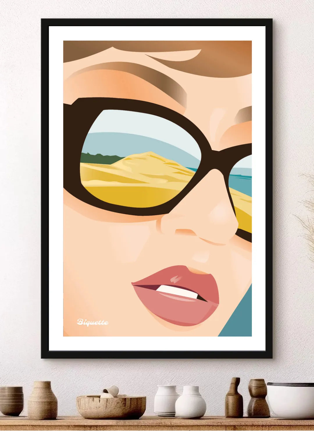 Affiche de la Dune du Pilat avec cadre noir minimaliste posée sur un buffet en bois sombre, entourée de poteries artisanales dans une ambiance intérieure chaleureuse et sobre.