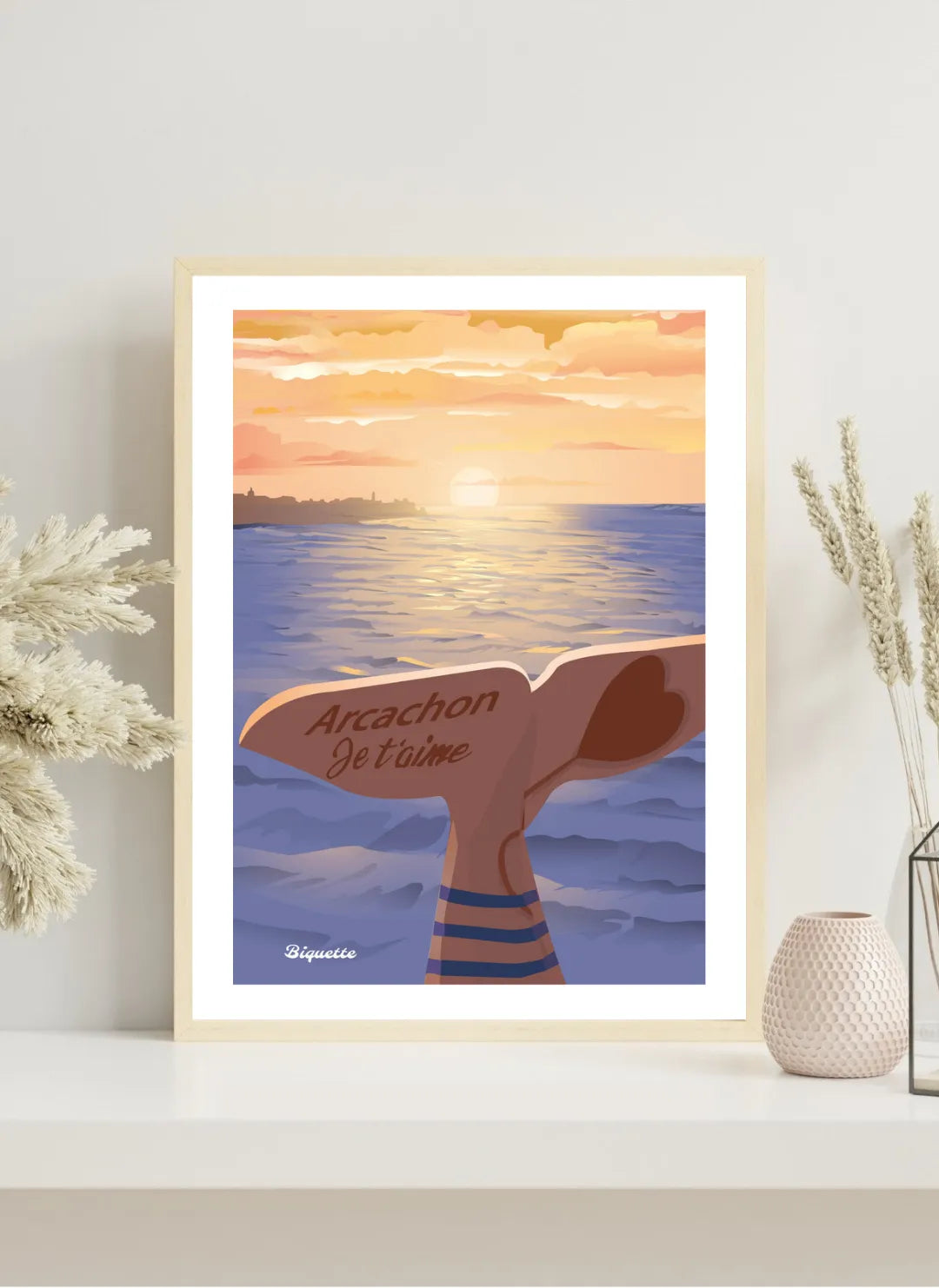 Poster "Arcachon Je t'aime" dans un cadre en bois clair, exposé sur une étagère minimaliste blanche à côté de fleurs séchées et d'un vase alvéolé.