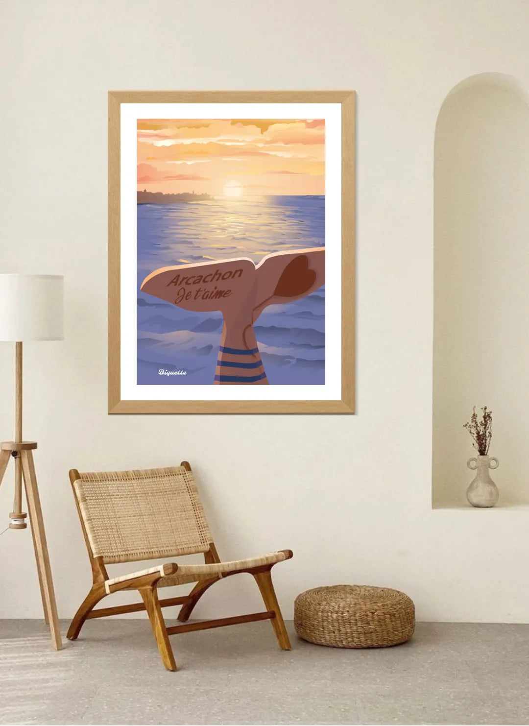 Illustration Arcachon Je t'aime encadrée en bois naturel dans un intérieur de style bohème épuré, avec une alcôve murale, un fauteuil en rotin et un luminaire sur pied.