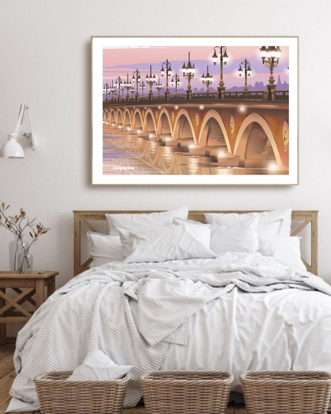 Affiche encadrée du Pont de Pierre à la lumière rose et orangée, suspendue dans une chambre à coucher claire au-dessus d'un lit blanc.
