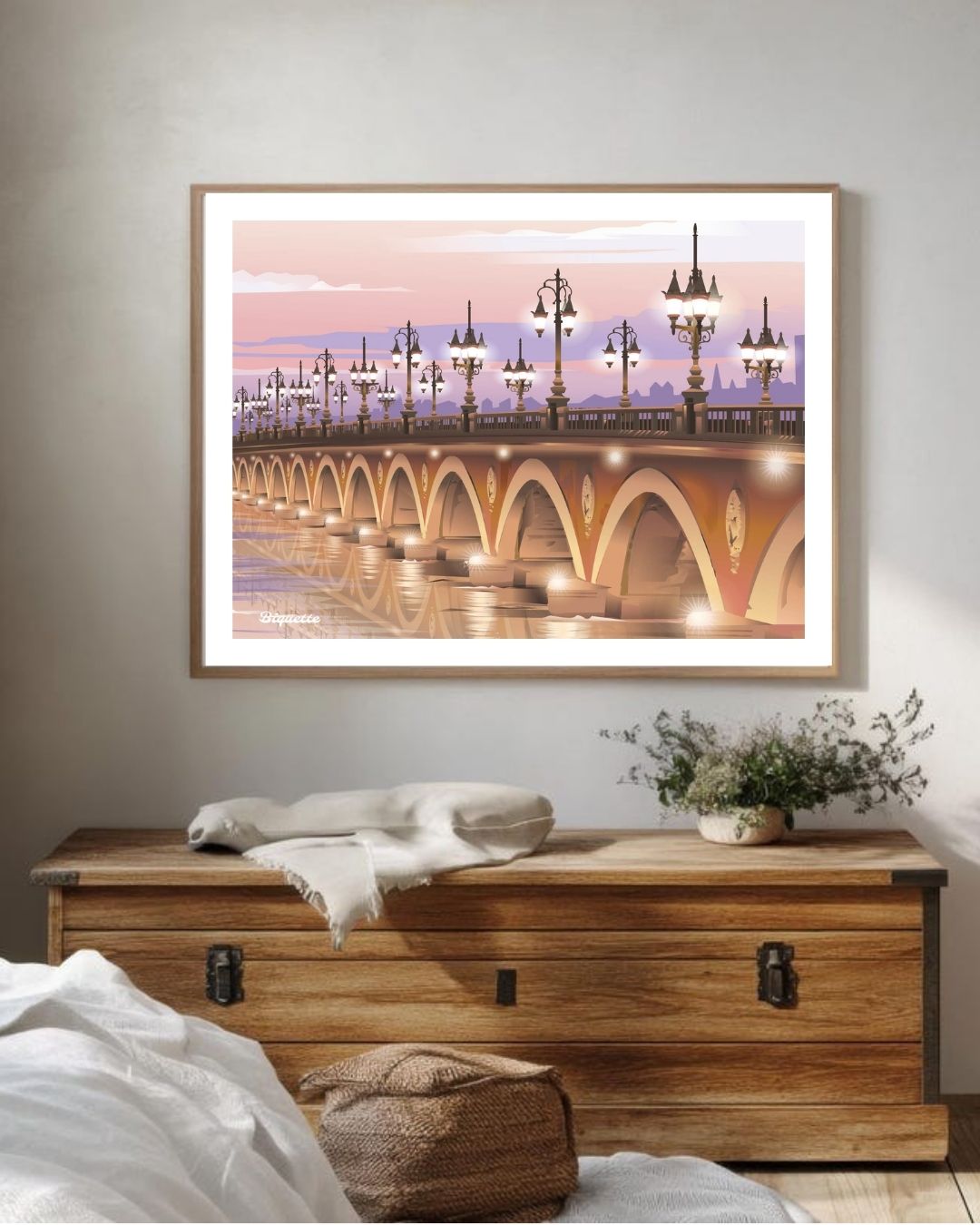 Illustration néo-rétro du Pont de Pierre de Bordeaux au crépuscule, encadrée et installée au-dessus d'une commode en bois brut rustique.