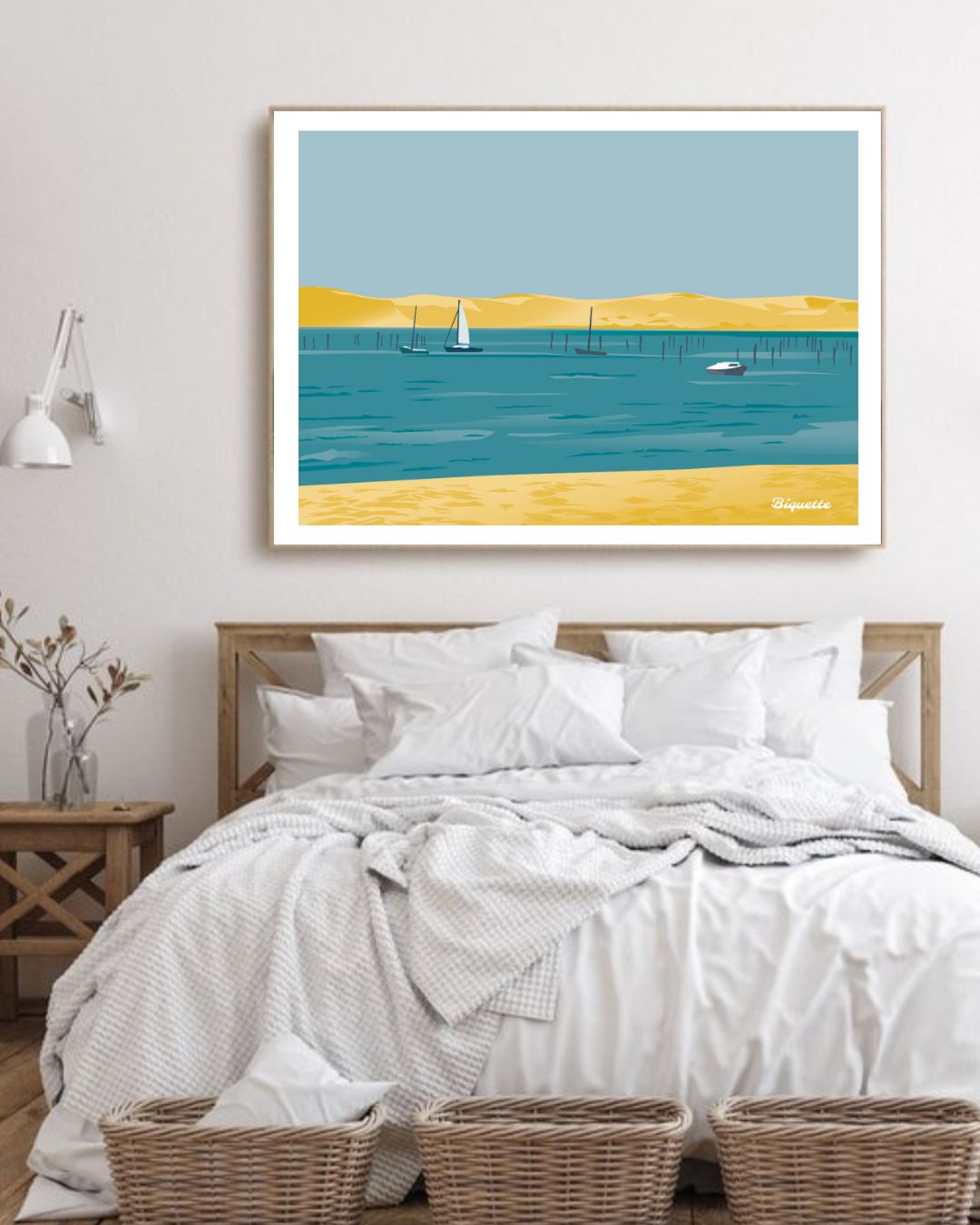 Affiche encadrée du paysage de mer et de plage du Cap Ferret, suspendue dans une chambre à coucher claire au-dessus d'un lit avec du linge blanc.