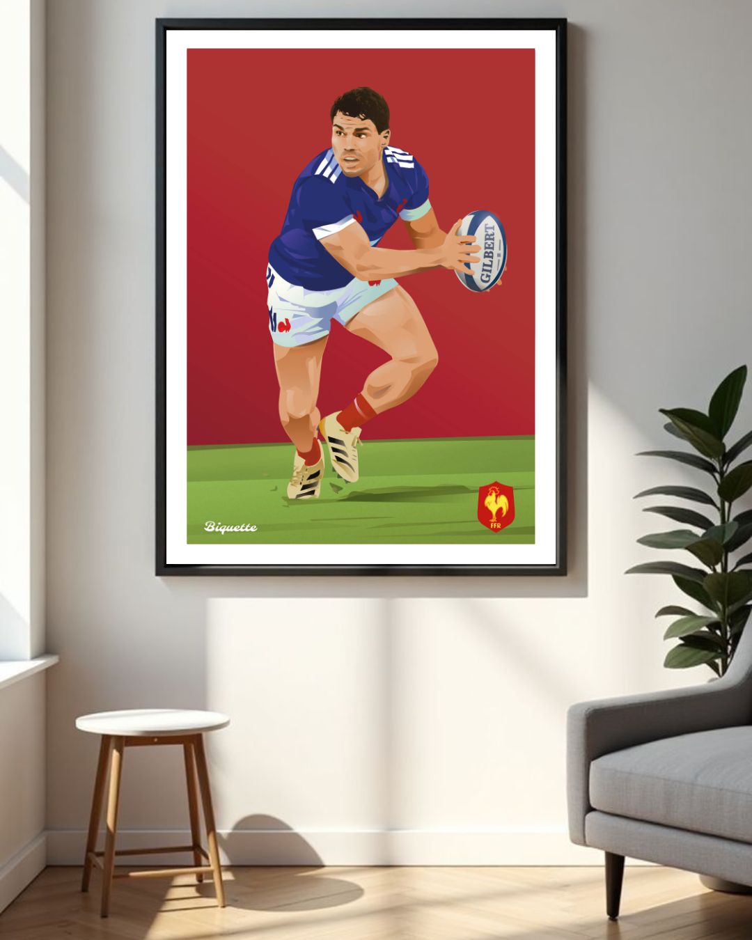 Affiche encadrée d'Antoine Dupont sous le maillot du XV de France suspendue dans un intérieur moderne à côté d'une plante verte et d'un fauteuil gris.