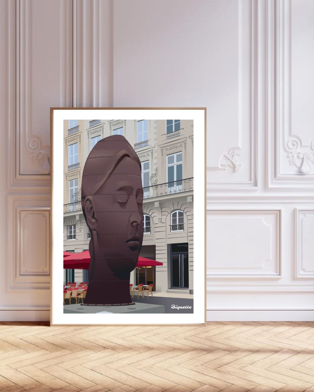 Grand cadre en bois clair avec l'affiche de la statue Sanna de Bordeaux, posé au sol contre un mur blanc orné de moulures haussmanniennes élégantes.