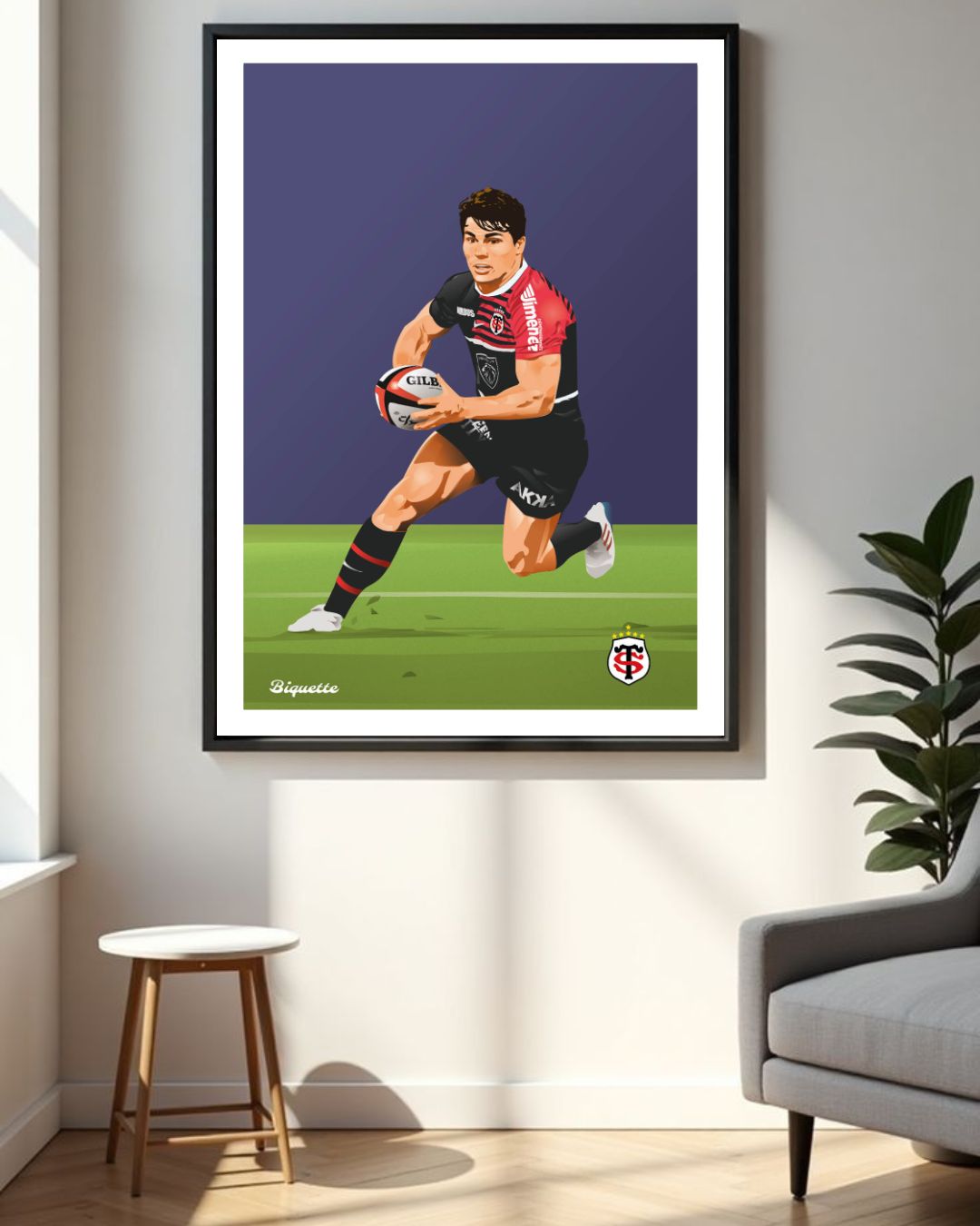 Grand poster du joueur du Stade Toulousain Antoine Dupont mis en valeur dans un cadre noir sur un mur blanc, à côté d'un fauteuil gris moderne.