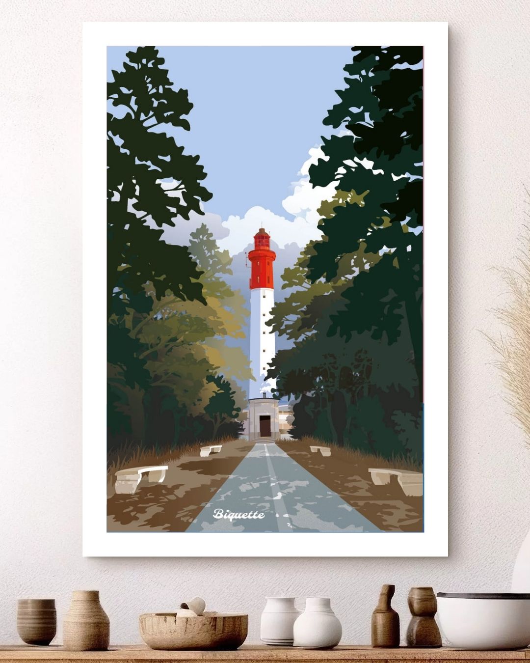 Affiche du Phare rouge et blanc du Cap Ferret signée Monsieur Biquette, encadrée au-dessus d'une étagère garnie de poteries et céramiques artisanales.