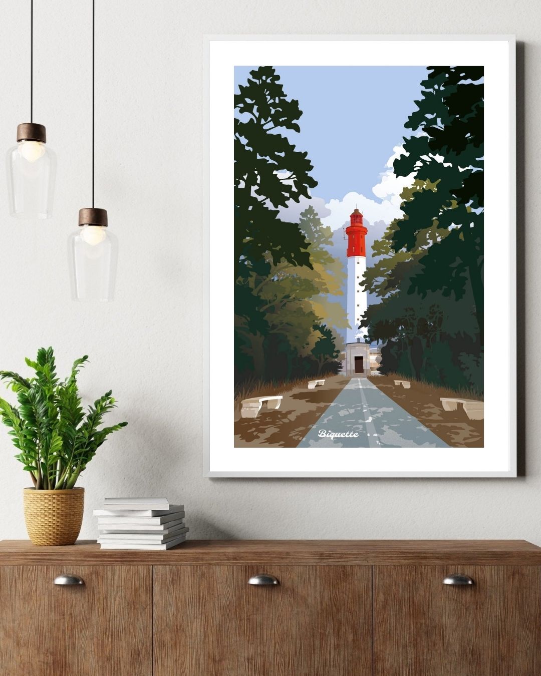 Illustration du Phare du Cap Ferret dans un cadre en bois, suspendue au-dessus d'un buffet en bois rustique à côté d'une plante verte en pot.